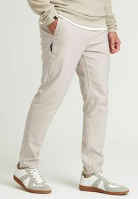 Lichtbeige broek met een slanke pasvorm, voorzien van zijzakken en een gladde textuur. Gekocht bij grijze en witte sneakers.
