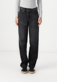 Black denim jeans with a straight leg design, five-pocket styling, and minimal fading. Styled with a grey ribbed long-sleeve top and black sneakers.