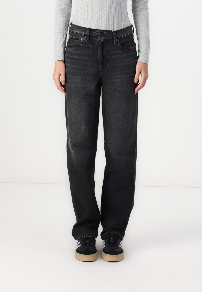 Black denim jeans with a straight leg design, five-pocket styling, and minimal fading. Styled with a grey ribbed long-sleeve top and black sneakers.