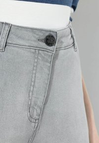 šedé džíny z denimu s hladkým povrchem, s černým zapínáním na knoflík, poutky na opasek a jemnými švy poblíž kapes.
