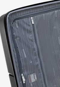 Intérieur d'une valise rigide noire comportant un tissu gris avec des motifs d'avion, une poche zippée en maille et des tirettes de fermeture éclair en métal.