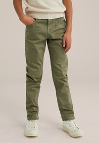 Groene katoenen chino's met een slim fit, voorzien van een middelhoge taille en opgerolde manchetten, gecombineerd met witte veterschoenen.