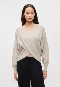 Top bej, tricotat cu burduf, cu mâneci lungi și design în V, combinat cu pantaloni negri. Materialul are o textură netedă.