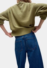 Olivově zelený texturovaný svetr s kleslými rameny spárovaný s modrými džíny s vysokým pasem, které mají zadní kapsy a volný střih.