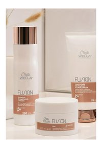 De Wella Fusion haarverzorgingsset bevat een witte shampoo-fles met een rosegouden dop, een witte maskerpot en een witte conditioner-tube, allemaal gelabeld.