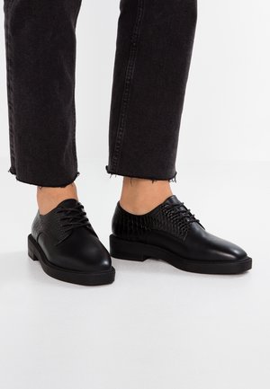 Chaussures en cuir noir avec un design texturé et tissé sur le dessus, bout rond et un talon bas empilé avec un détail en lacets.