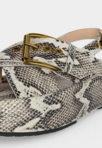 Μοντέρνο πέδιλο πλατφόρμας με λευκό και μαύρο σχέδιο φολιδωτού δέρματος φιδιού, χρυσή αγκράφα και ρυθμιζόμενο λουράκι.