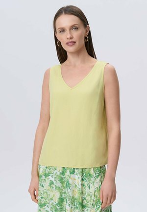 Top sin mangas amarillo limón con cuello en V y un corte relajado, hecho de tejido ligero. Llevado con una falda de estampado floral en verde y blanco.