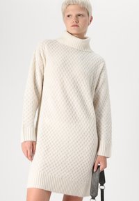 Πλεκτό φόρεμα σε ελεφαντόδοντο με υφή κηρήθρας, ψηλό γιακά και ριμπ μανίκια. Μήκος μέχρι το μεσαίο μέρος του μηρού, χαλαρή εφαρμογή, με λεία φινίρισμα.