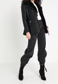 Chaqueta negra de cuero acolchada con cuello de piel, llevada sobre una camiseta blanca. Combinada con pantalones jogger negros de cintura alta y botines negros con tacón y cordones.