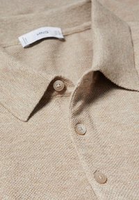 Polo shirt en tricot beige avec un col doux et trois boutons assortis le long de la patte de boutonnage.