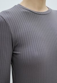Top grigio a maniche lunghe realizzato in tessuto a coste. Presenta un collo rotondo e una vestibilità slim, evidenziando linee verticali in diverse tonalità di grigio.