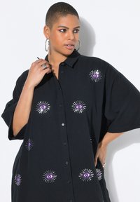 Zwarte oversized button-up shirt met reliëf paarse oogontwerpen en zilveren stralen, met een gestructureerde stof en korte mouwen.