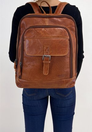 Brown leather backpack with a smooth texture, rectangular shape, front pocket with a buckle closure, and side zipper compartments.