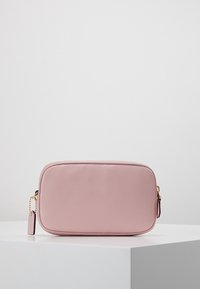 Suuri vaaleanpunainen nahkalaukku, jossa on nyppyläinen pinta, kullanväriset yksityiskohdat ja vetoketjulla suljettavat osat. Mukana on pieni tage, joka on kiinnitetty ketjulla.