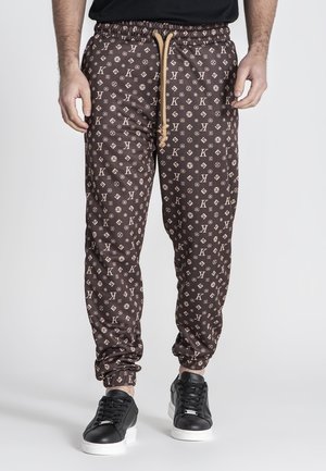 Pantalones jogger marrones con un diseño estampado y cintura con cordón, con un logotipo, tobillos ajustados y combinados con zapatillas negras.