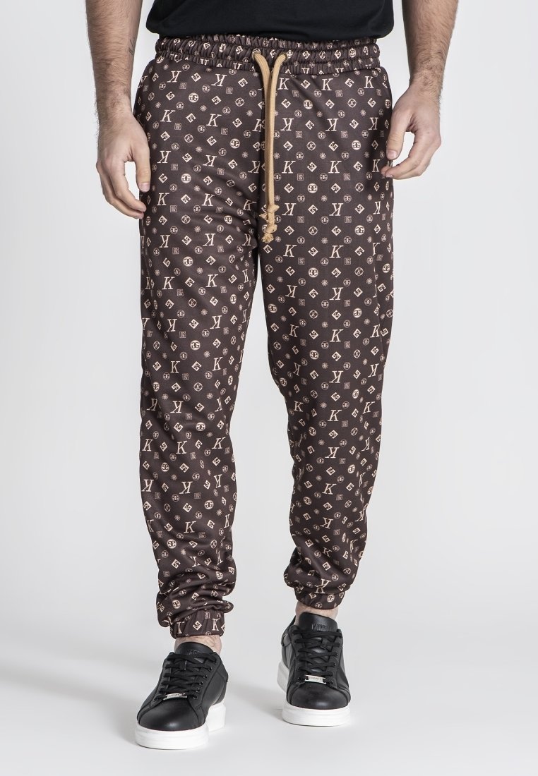 Pantalones jogger marrones con un diseño estampado y cintura con cordón, con un logotipo, tobillos ajustados y combinados con zapatillas negras.