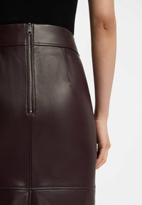 Gonna a matita in pelle marrone con una superficie liscia, dotata di cerniera sul retro e cuciture sartoriali. La vita è strutturata e aderente.
