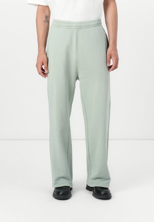 Hellgrüne, schmal zulaufende Sweatpants mit einem elastischen Bund, seitlichen Taschen und einem glatten Baumwollstoff. Getragen mit schwarzen Schuhen.