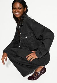 Fekete farmerdzseki ezüst gombokkal, laza fekete nadrággal és csatokkal díszített bordó cipővel párosítva. Szövet textúra végig.