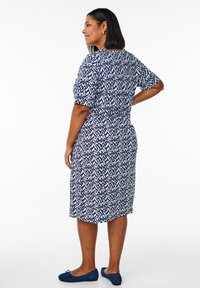 Ein navy- und weißes gemustertes Kleid mit kurzen Ärmeln, tailliertem Schnitt und knielangem Design, kombiniert mit blauen flachen Schuhen.