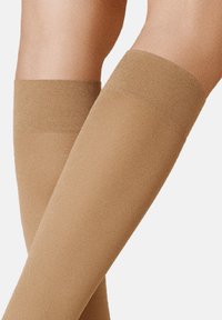 Beige, knielange Strümpfe mit glatter Textur und einem gerippten oberen Bündchen. Sie haben ein tailliertes Design, das sich an das Bein anpasst.