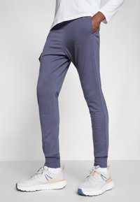 Graublau Jogginghosen mit Seitentaschen, tailliertem Design, gerippten Bündchen und glatter Textur, kombiniert mit weißen Sportschuhen.