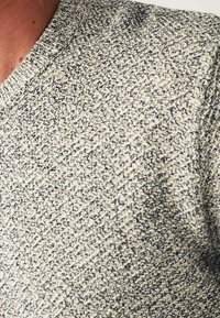 Gros plan sur un pull à col rond en maille avec un motif texturé en fils beige et bleu foncé.
