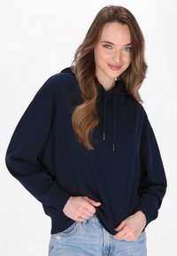 Pulover cu glugă de culoare bleumarin, cu o croială lejeră, șnur și manșete ribbate, asortat cu blugi de denim decolorat.