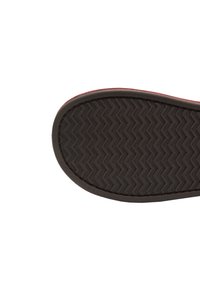 Suela de un zapato marrón con un patrón de zigzag texturizado en la parte inferior, aislada sobre un fondo blanco.