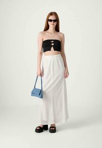 Top preto sem alças com três recortes frontais, saia maxi texturizada branca, bolsa azul, sandálias plataforma pretas e óculos de sol.