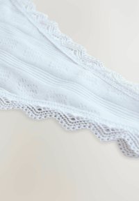 White lace-trimmed fabric features a striped texture and intricate patterns. The edge displays a delicate scalloped design.