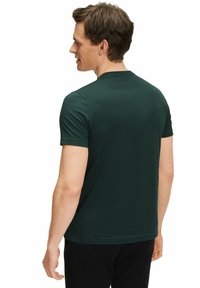 Maglietta a maniche corte verde scuro realizzata in tessuto morbido, con colletto girocollo classico e design aderente, indossata da un modello maschile visto da dietro.