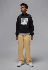 Black hooded sweatshirt with a large white Jordan logo, paired with beige cargo pants featuring side pockets and white sneakers with mint accents.