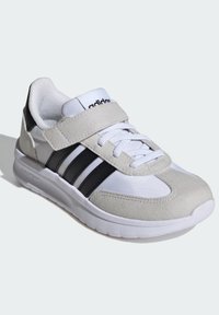 Baskets de sport avec une tige en mesh blanc et en suédé, des rayures noires et une sangle Velcro. Présentent une semelle rembourrée et des éléments de design texturés.