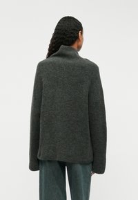 Tummanharmaa neulottu villapaita, jossa on korkea kaulus, rento istuvuus ja teksturoitu pinta. Yhdistetty vaaleansinisiin löysiä farkkuihin.