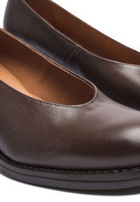 Zapatos de cuero marrón con una textura suave, punta redondeada y paneles laterales elásticos. Presentan un ribete cosido a lo largo de la suela.