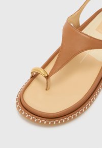 Sandale en cuir tan avec une accentuation dorée, un surfil crème le long de la semelle, et une semelle intérieure beige lisse.