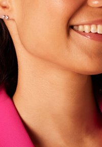 Boucles d'oreilles en argent avec un design géométrique, ornées de pierres précieuses transparentes. Gros plan sur la peau et la zone du cou, portant des vêtements rose vif.