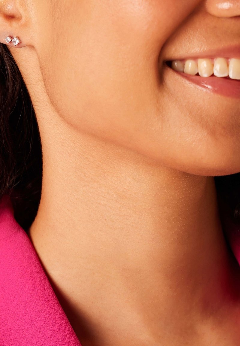 Boucles d'oreilles en argent avec un design géométrique, ornées de pierres précieuses transparentes. Gros plan sur la peau et la zone du cou, portant des vêtements rose vif.