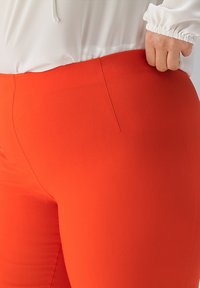 Hoch sitzende Hose in leuchtendem Rot, aus einem glatten, dehnbaren Material gefertigt. Verfügt über eine Seitentasche und ein figurbetontes Design.