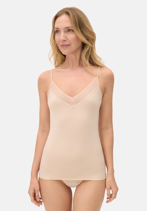 Mujer con cabello rubio, vistiendo un camisón color nude con tirantes delgados y decoración de encaje, posando frente a un fondo blanco liso.