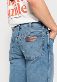 Ljust blå denimjeans med en brun läderetikett från Wrangler, med bakfickor som har zigzag-stygn och en standardpassform.