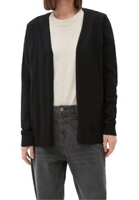 Svart cardigan med öppen framsidan, långa ärmar, ribbade mudd och texturerat stickat tyg, bärs ovanpå en ljus skjorta och mörka jeans.