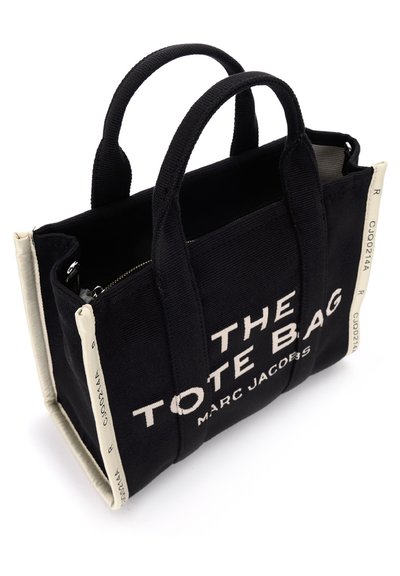 Must mustritoot bag, millel on kreemikad aktsendid, lukuga sulgemine ja julge valge tekst, mis ütleb "THE TOTE BAG MARC JACOBS." Kahekordne kangast käepide.