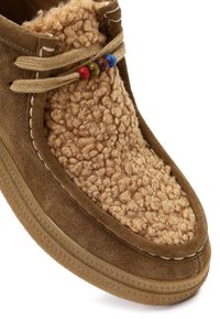 Brązowe zamszowe buty z teksturowaną, puszystą górą w kolorze jasnobrązowym, zdobione dekoracyjnymi, wielokolorowymi koralikami na sznurówkach. Solidna gumowa podeszwa z kontrastującymi szwami.