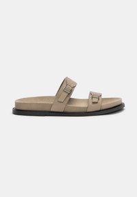 Beige suede slide sandal featuring two adjustable straps with silver hardware, flat black sole, and a cushioned footbed for comfort.