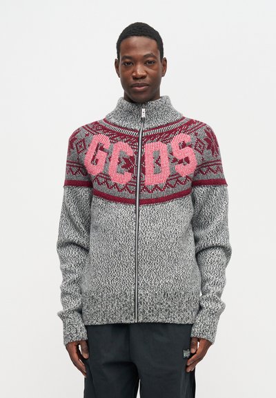 Grijze gebreide zip-up trui met een hoge kraag, voorzien van een kastanjebruine patroon bij de schouders en "GEOS" in grote roze letters op de borst.