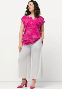 Fuchsia Oberteil mit weißem Palmenblattmuster, V-Ausschnitt, kurze Ärmel; kombiniert mit weißen weiten Hosen und rosa High-Heels.