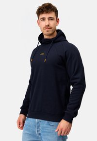 Navy hoodie lavet af blødt stof, med en snor med orange spidser, ribbede manchetter og et logo på brystet, stylet med afslappet pasform.